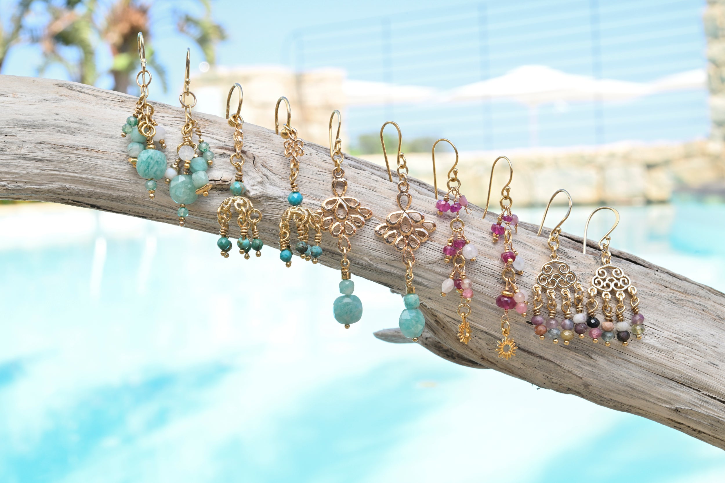 Gold and beaded gemstone earrings hanging on a branch with a blurred natural background.