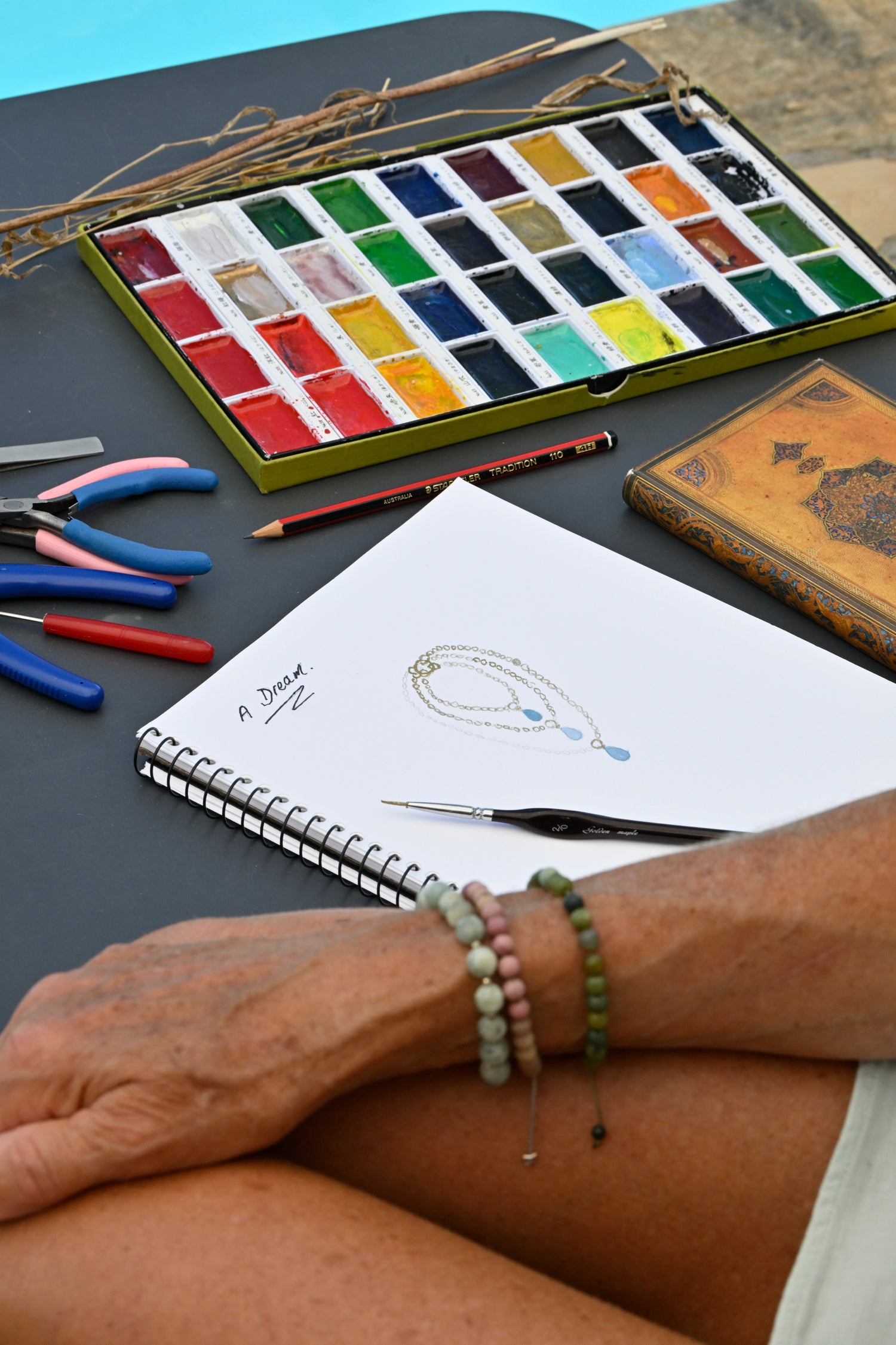 Artistic setup with watercolor paints, brushes, and a sketchbook on a table.