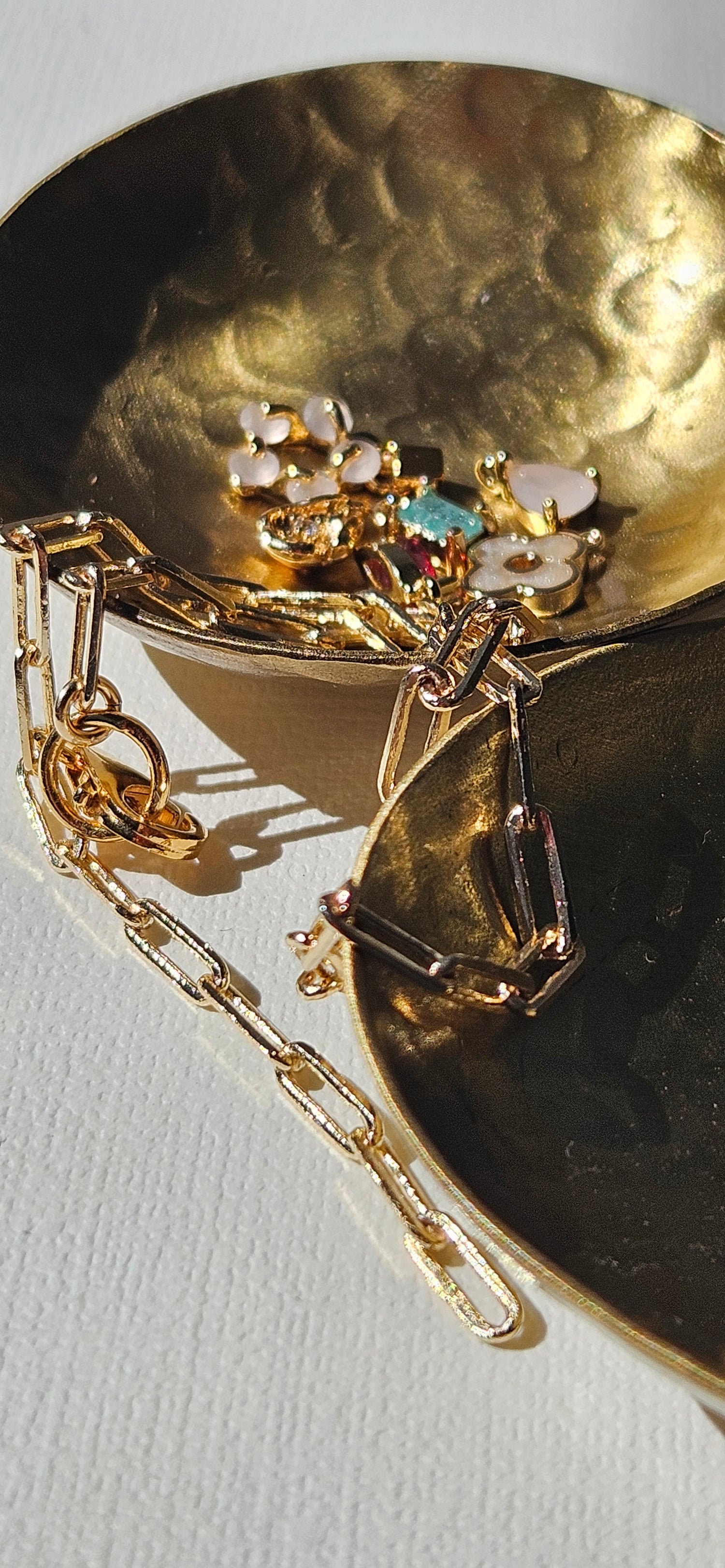 Gold necklace with various pendants on a light grey background.