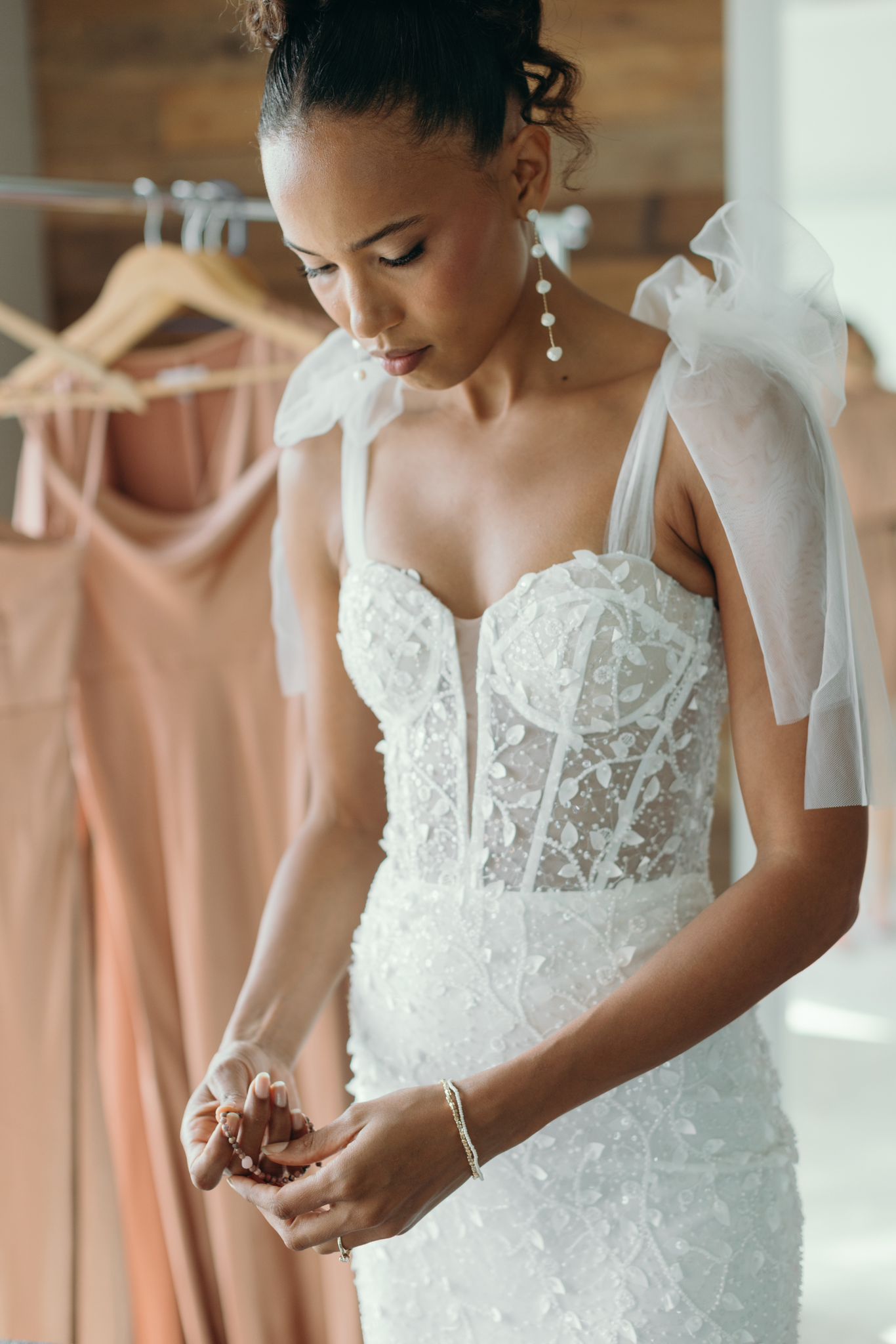 Woman in a white lace wedding dress with a veil, standing in front of a rack of dresses wearing a Soul & Stone bracelet.