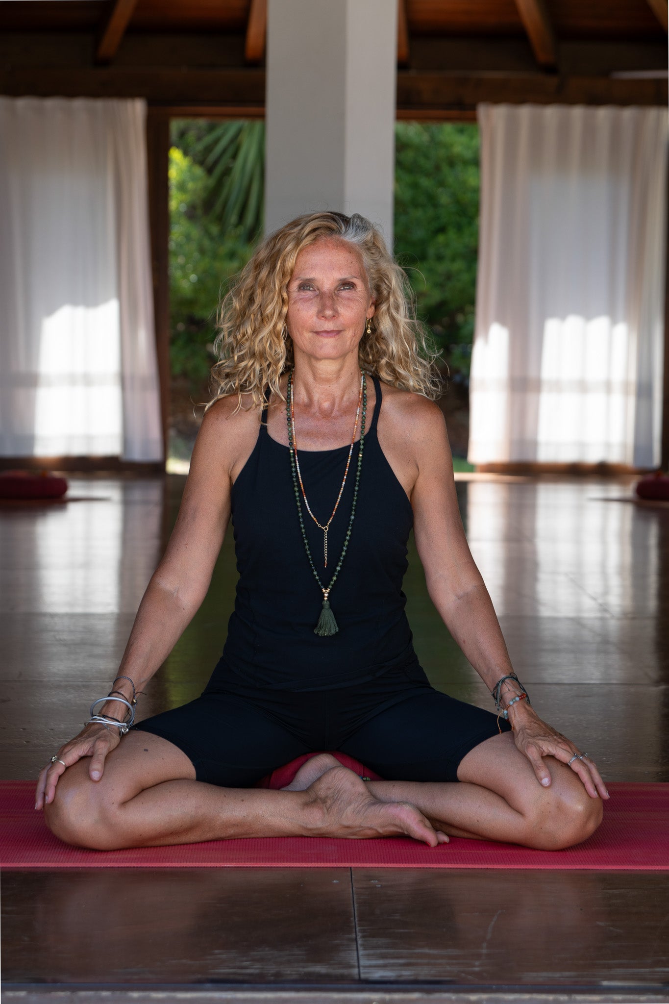 Woman in a yoga pose on a mat in a room wearing a gemsone lariat.