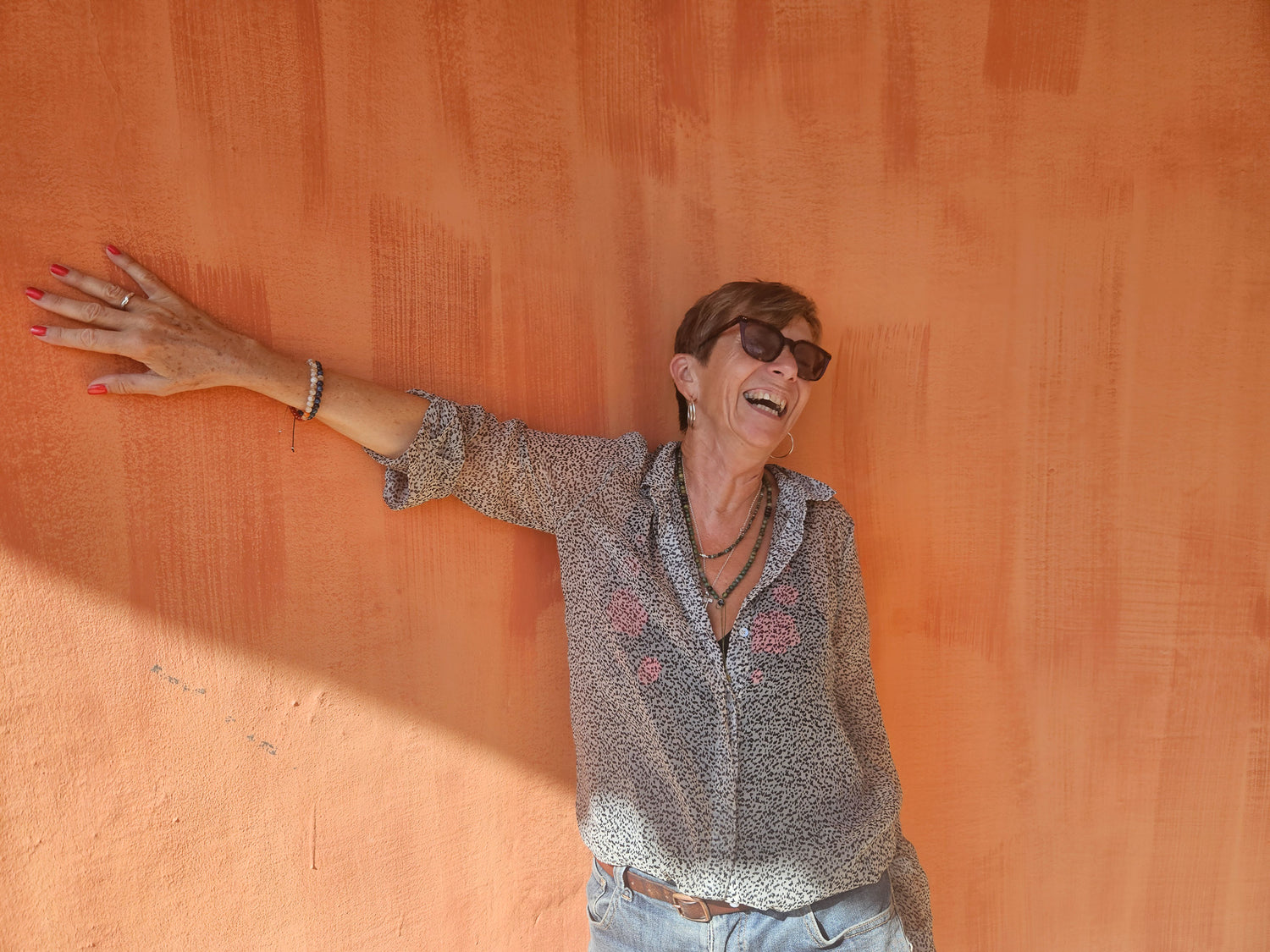 Woman with arms outstretched against an orange wall wearing a gemstone lariat and bracelets.