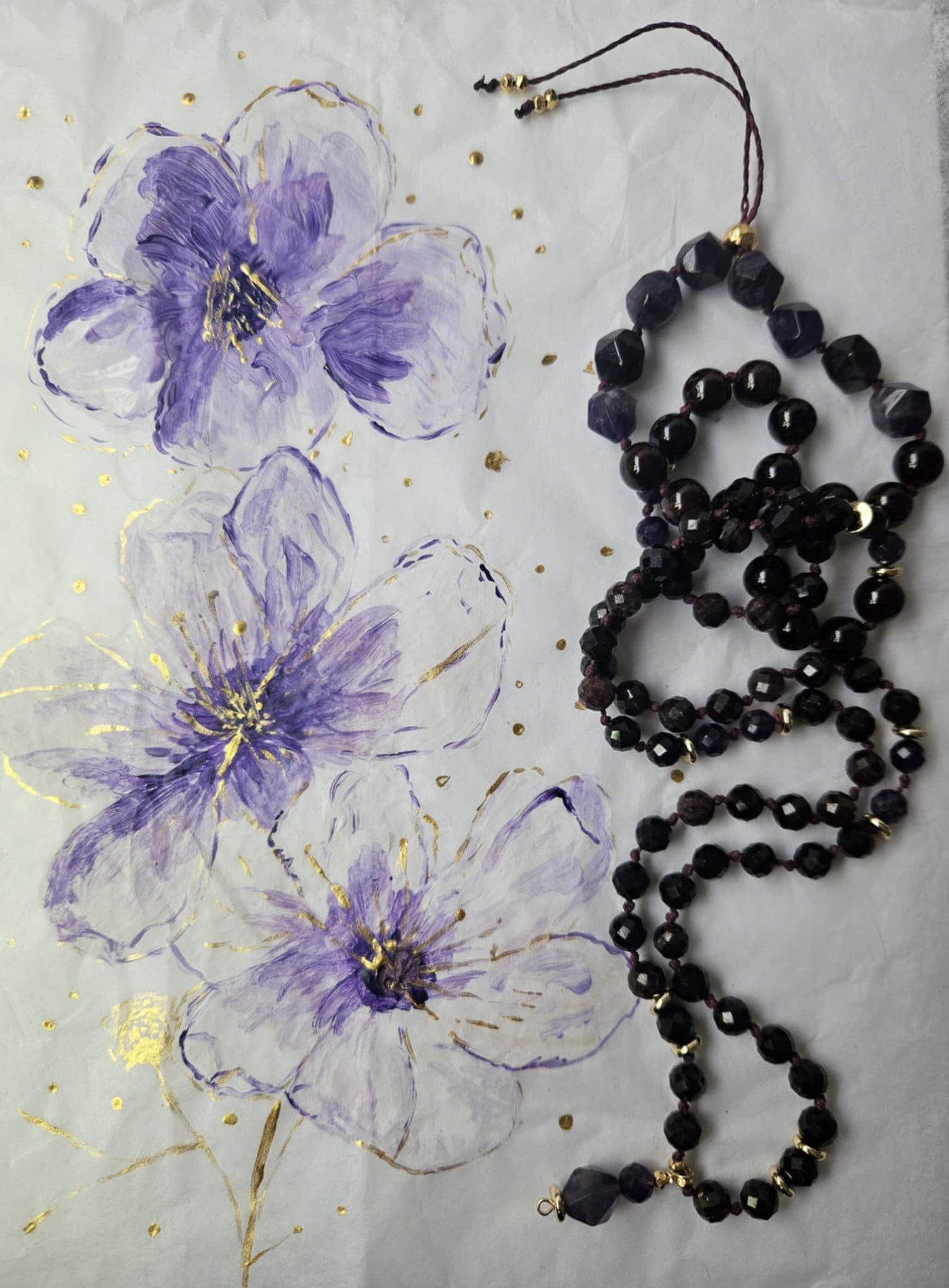Black beaded necklace on a textured surface with purple floral designs.