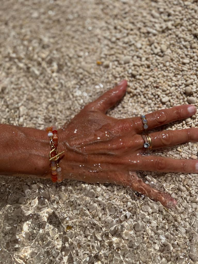 A woman's hand submerged in water on the shore adorned in Soul & Stone jewellery.