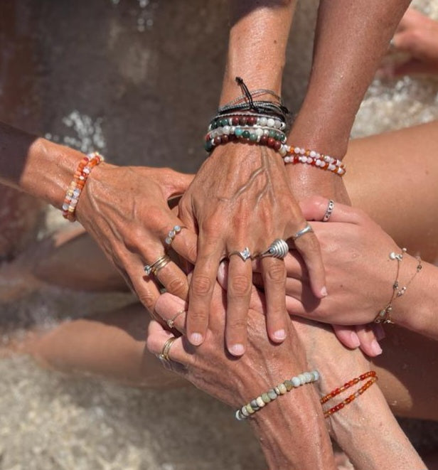A group of women's hands adorned in Soul & Stone jewellery touching above the water.